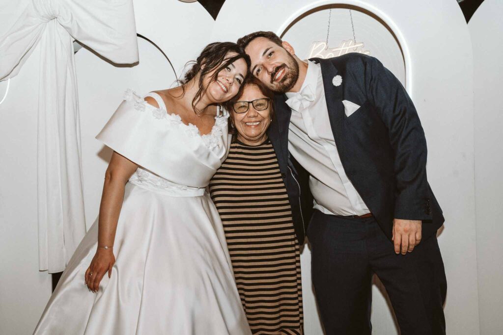 Brautpaar lehnt liebevoll die Köpfe an die Brautmutter für ein herzliches Gruppenfoto während der Hochzeitsfeier.