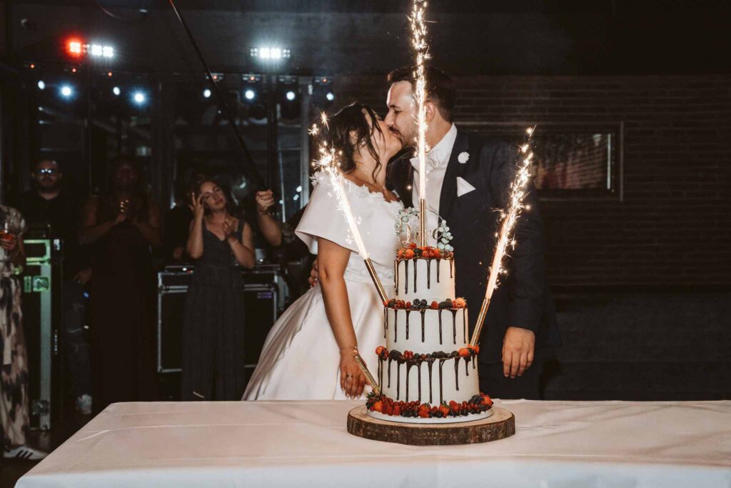 Braut und Bräutigam küssen sich vor ihrer Hochzeitstorte mit funkelnden Wunderkerzen während der Feier in Böblingen.