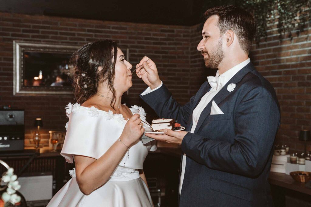Braut und Bräutigam füttern sich gegenseitig mit Hochzeitstorte während der Feier in Böblingen.