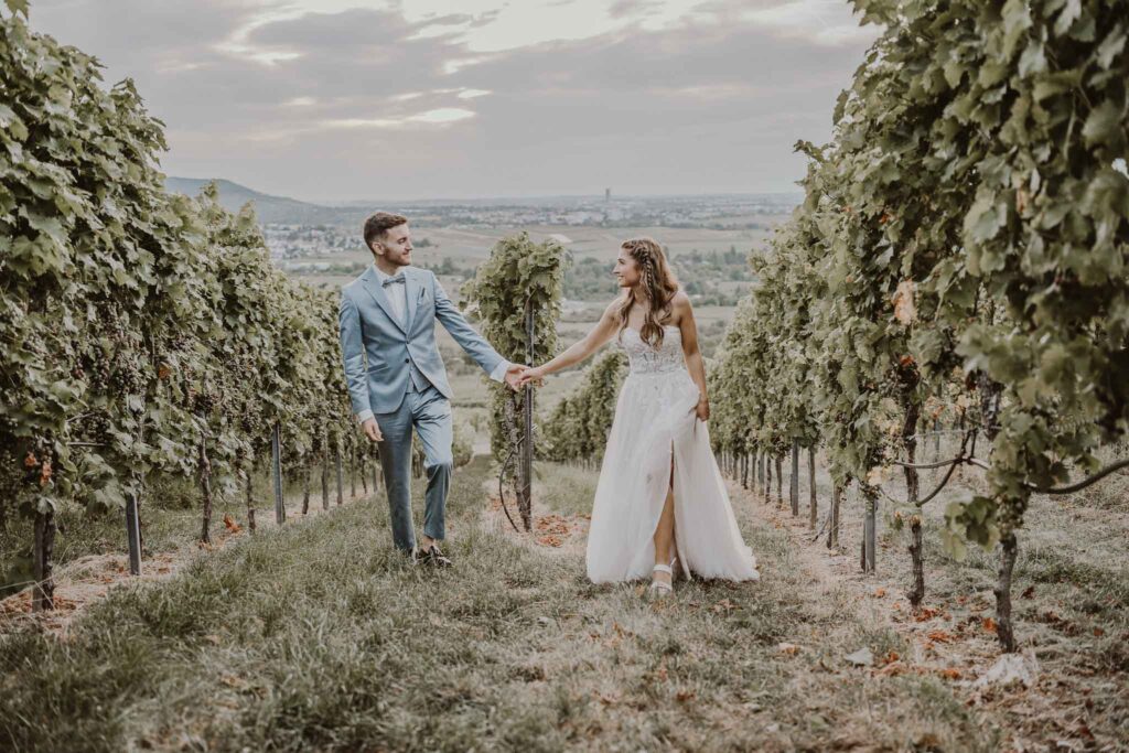 Paar, das sich an den Händen hält und durch einen Weinberg bei Esslingen geht, mit weiter Landschaft im Hintergrund.