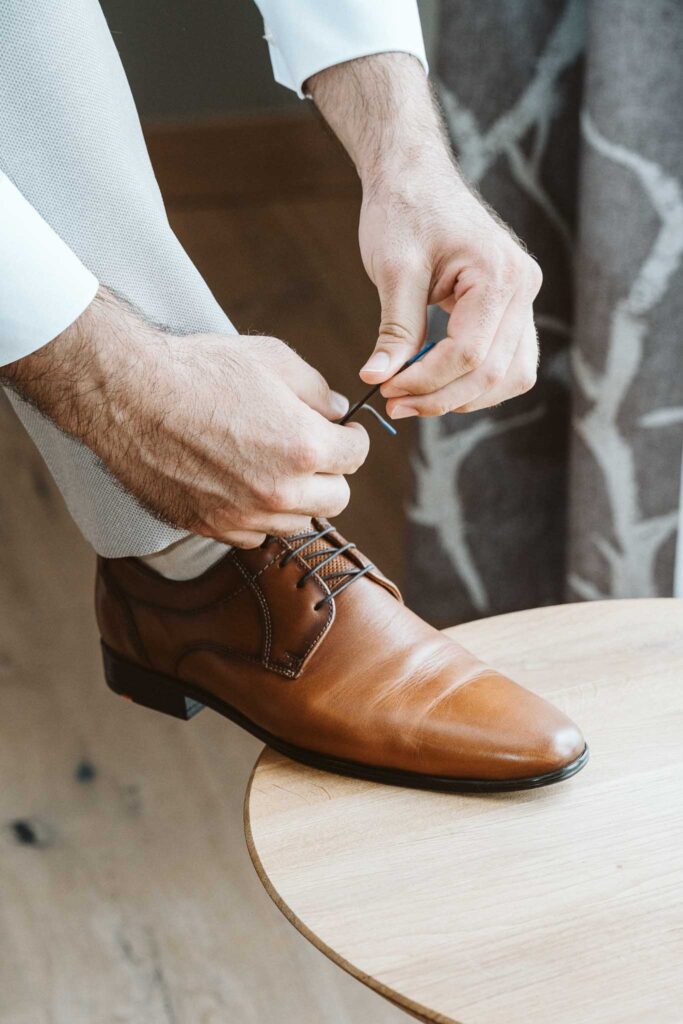 Bräutigam zieht sich beim Getting Ready seine braunen Lederschuhe an.