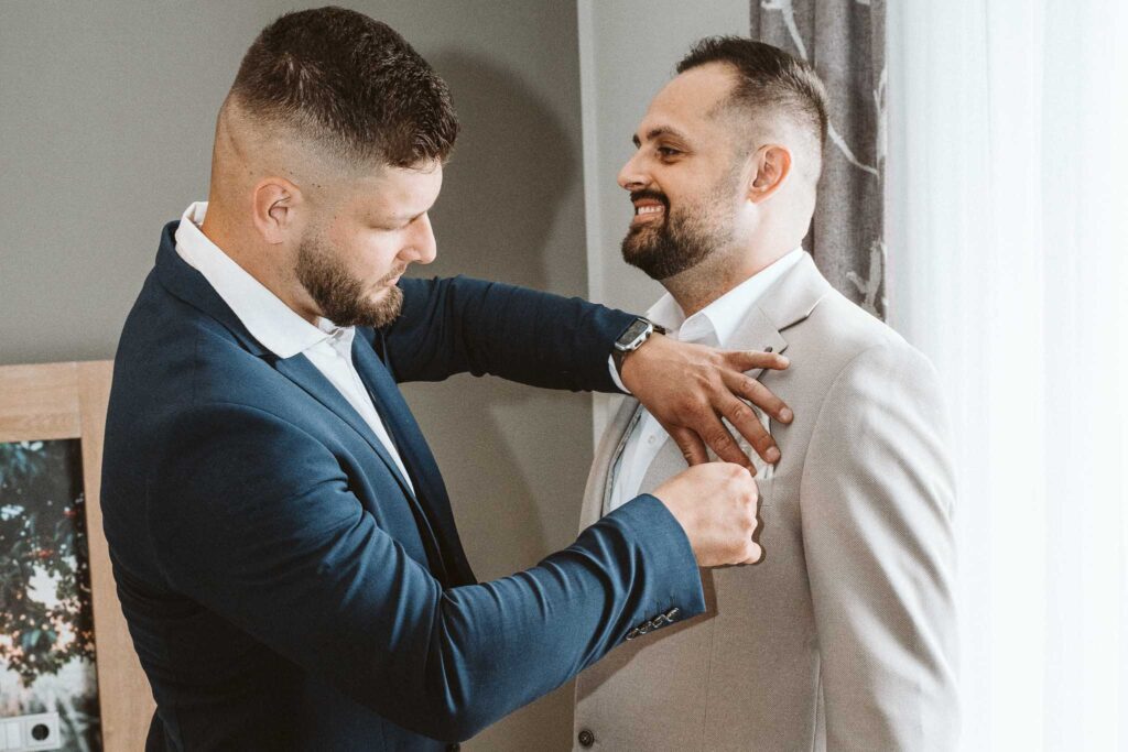 Trauzeuge richtet dem Bräutigam den Anzug beim Getting Ready am Hochzeitstag.