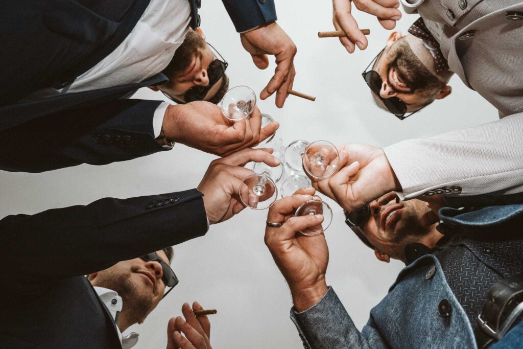 Groomsmen stoßen beim Getting Ready mit Getränken auf den Hochzeitstag an.