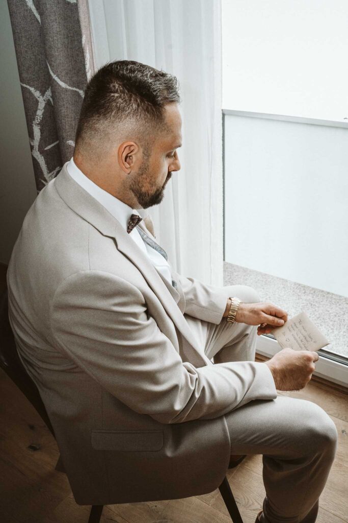 Bräutigam sitzt am Fenster und liest seine persönliche Nachricht beim Getting Ready in Breisach am Rhein.
