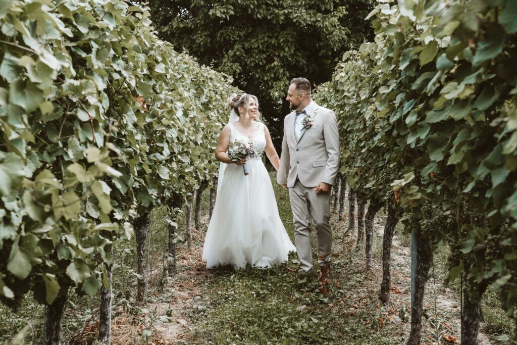Braut und Bräutigam spazieren Hand in Hand durch einen malerischen Weinberg in Breisach am Rhein während ihres Brautpaar-Shootings.