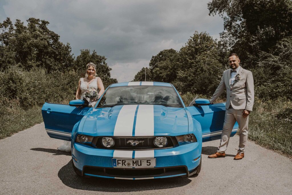 Brautpaar mit blauem Mustang auf einer Landstraße in Breisach am Rhein beim Hochzeitsshooting.