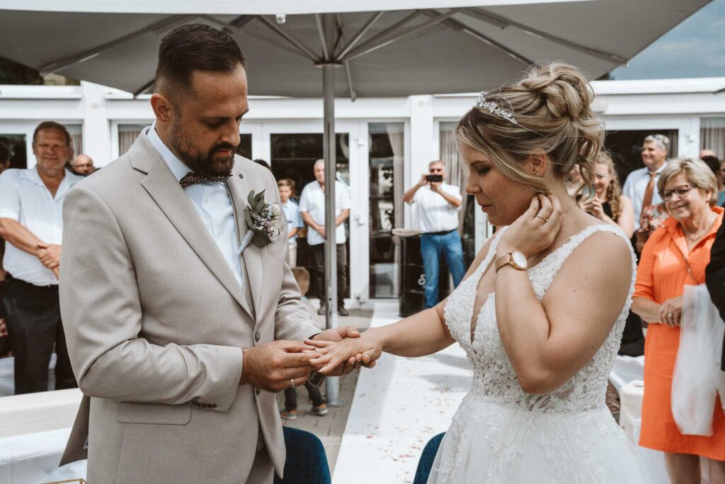 Braut und Bräutigam stecken sich während der freien Trauung in Breisach am Rhein gegenseitig die Ringe an, umgeben von ihren Gästen.