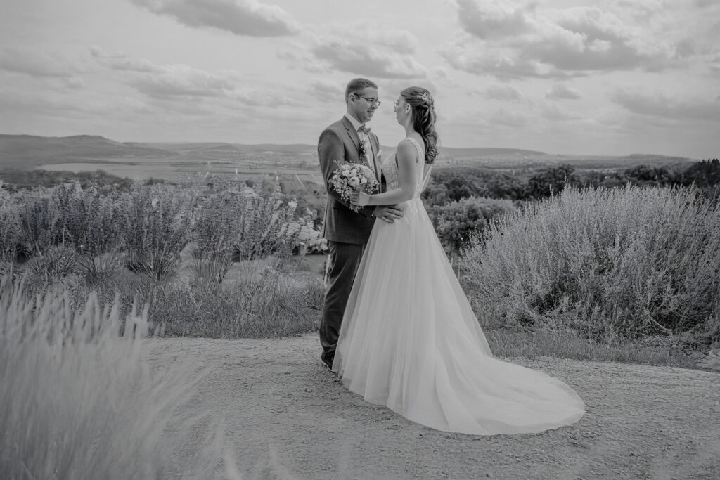 Ein Brautpaar steht eng umarmt auf einem Feldweg, umgeben von weiter Natur und leicht bewölktem Himmel in Affalterbach bei Ludwigsburg.