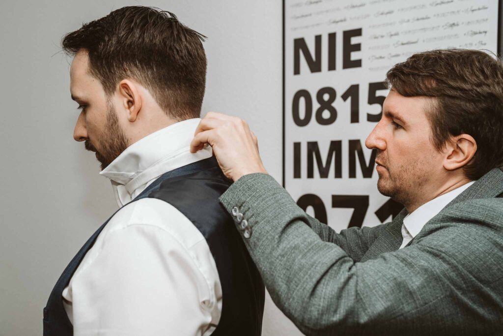 Trauzeuge hilft dem Bräutigam beim Anlegen des Kragens während des Getting Ready.