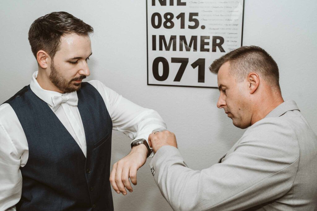 Bräutigam beim Getting Ready, unterstützt von seinem Trauzeugen, der ihm die Manschettenknöpfe anlegt.