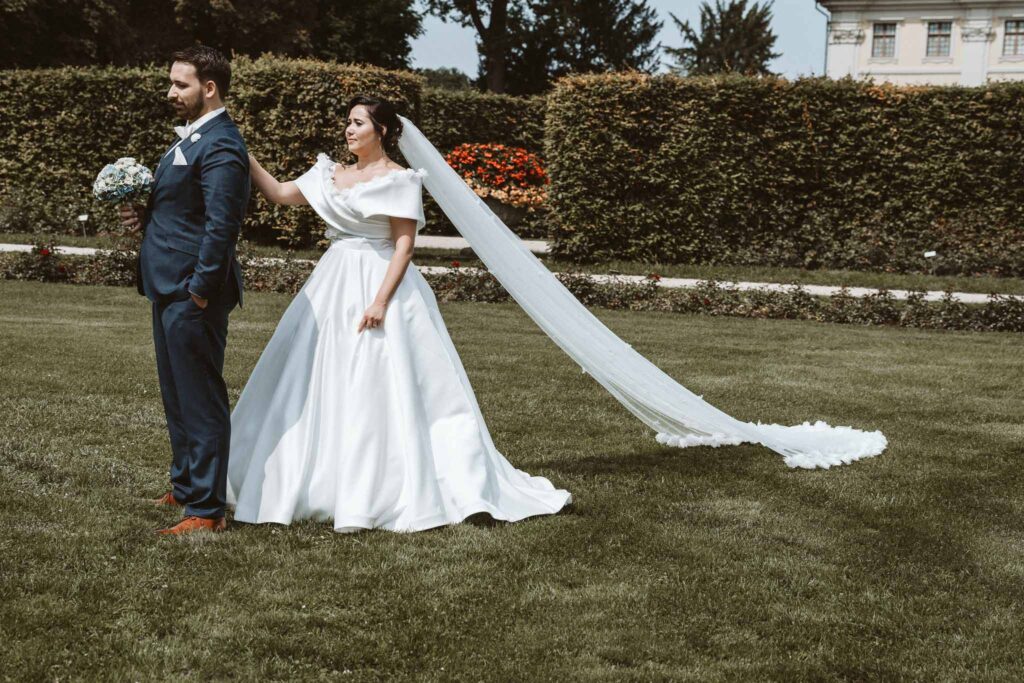 Braut tippt dem Bräutigam im Schlossgarten Ludwigsburg sanft auf die Schulter, um den First Look einzuleiten.