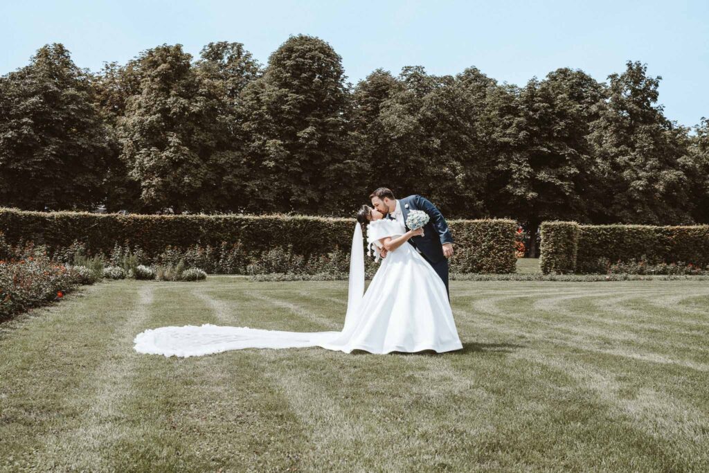 Brautpaar in inniger Pose im Schlossgarten des Residenzschlosses Ludwigsburg, eng umschlungen vor gepflegtem Grün.