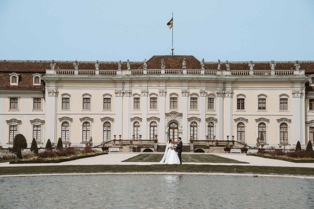 Weitwinkelaufnahme des Brautpaares vor dem prunkvollen Residenzschloss Ludwigsburg mit barocker Fassade.
