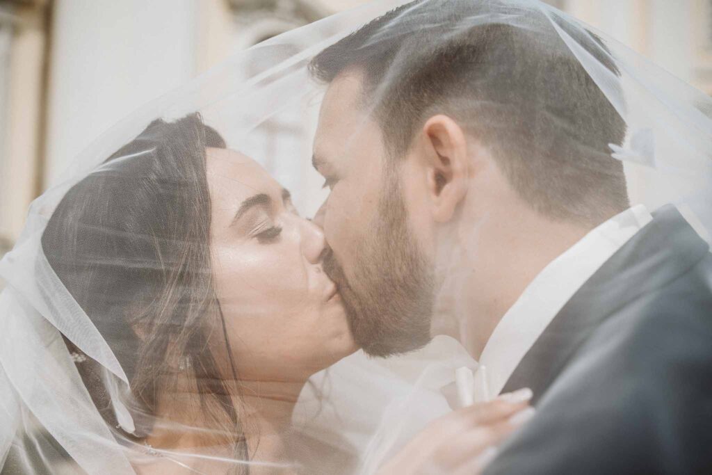 Braut und Bräutigam küssen sich hinter dem Brautschleier – romantischer Hochzeitsmoment im Schlossgarten von Ludwigsburg.