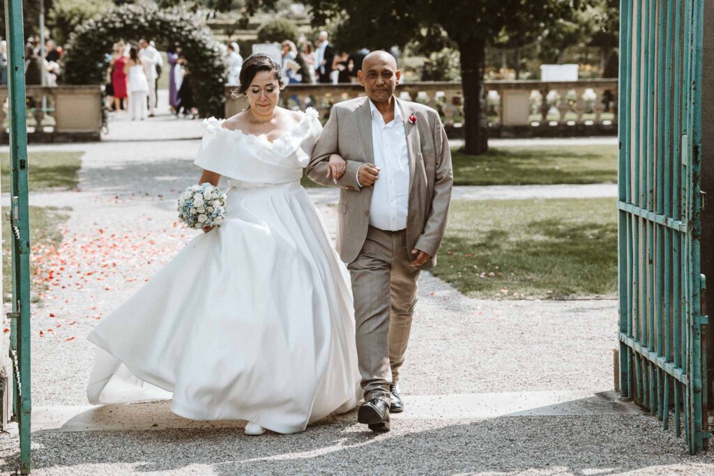 Braut wird von ihrem Bruder zur freien Trauung im Schlossgarten des Residenzschlosses Ludwigsburg geführt.