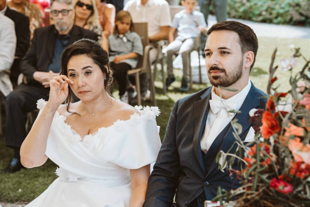 Emotionaler Moment während der freien Trauung, bei dem die Braut sich Tränen aus dem Gesicht wischt, während das Brautpaar gemeinsam vorne sitzt.