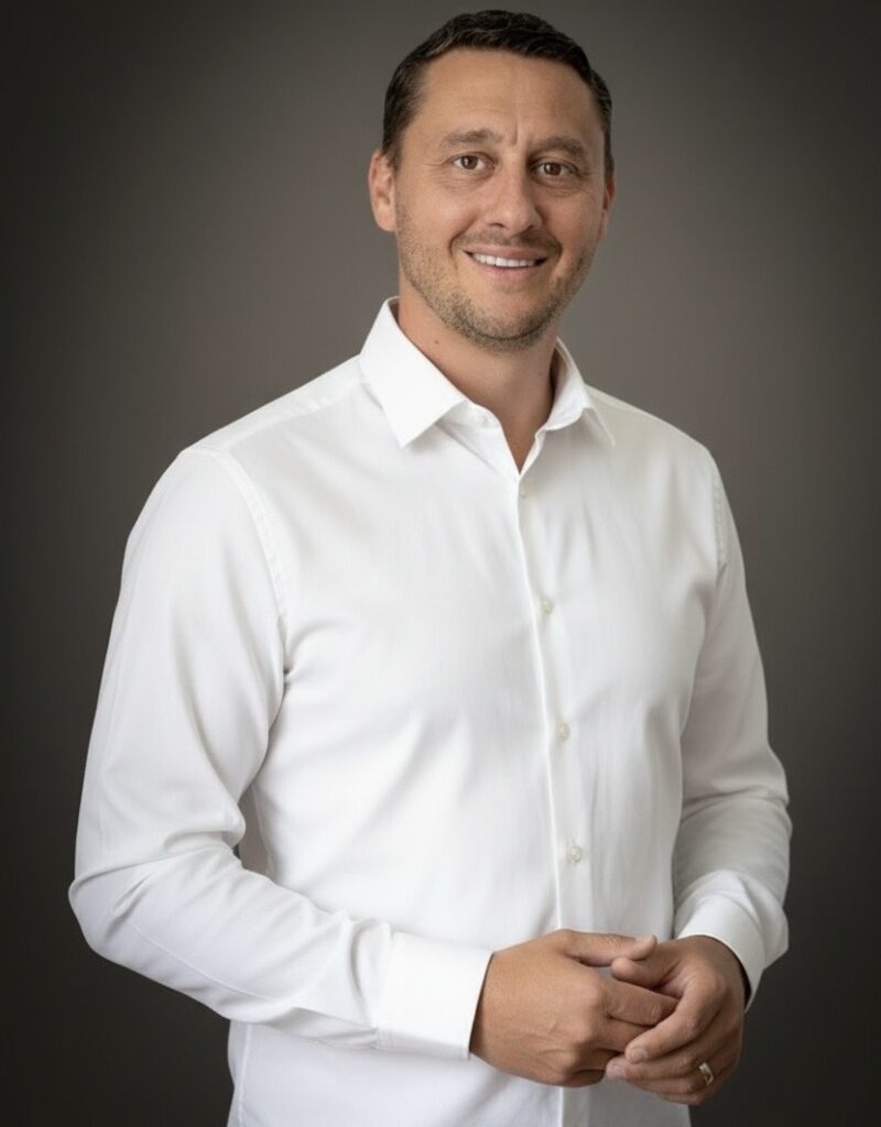 Business-Portrait eines Fotografen mit Kamera und Tragegurt vor neutralem Hintergrund.